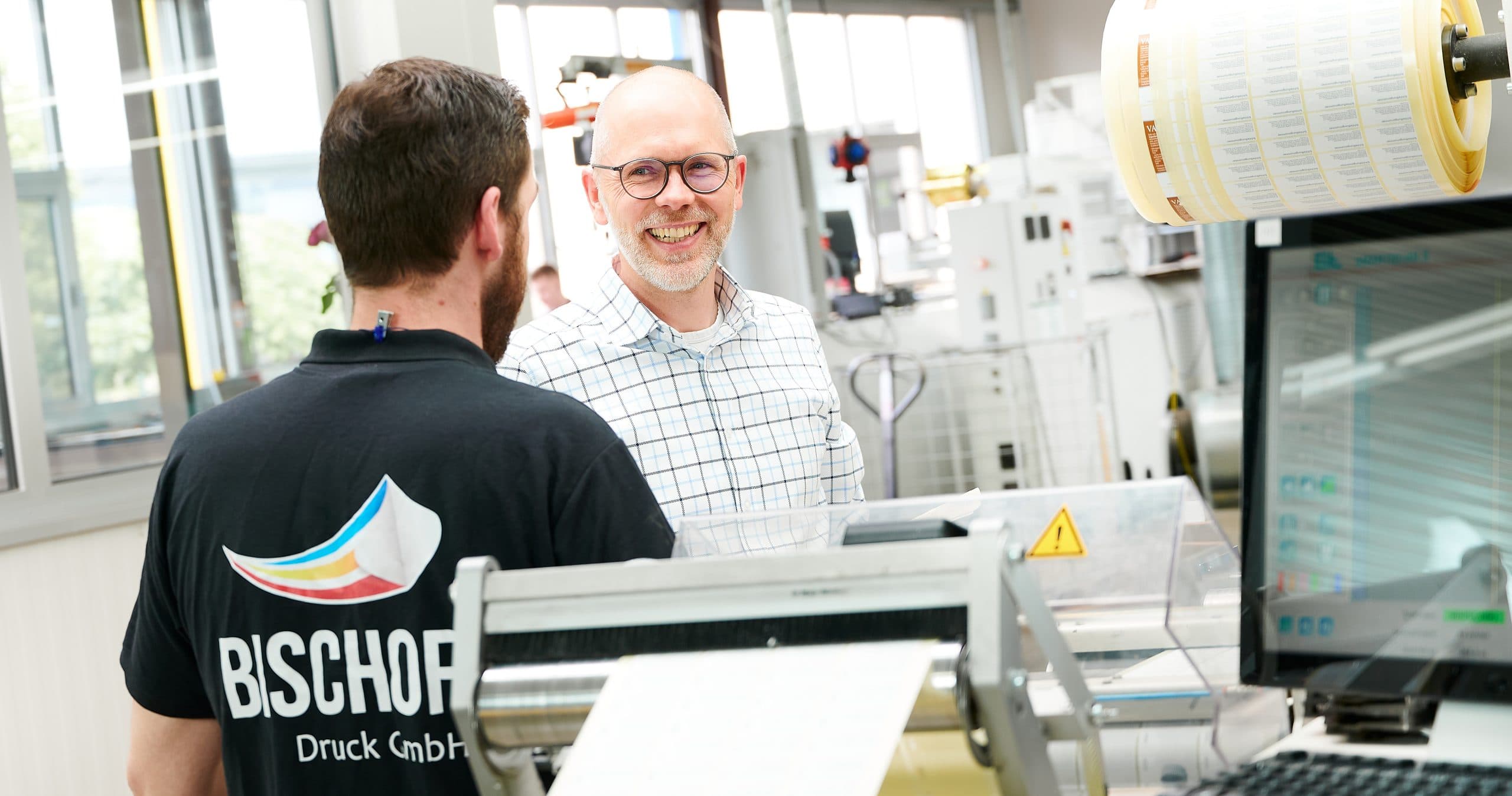 Geschäftsführung im Gespräch mit einem Mitarbeiter an der Produktionslinie bei Bischof Druck